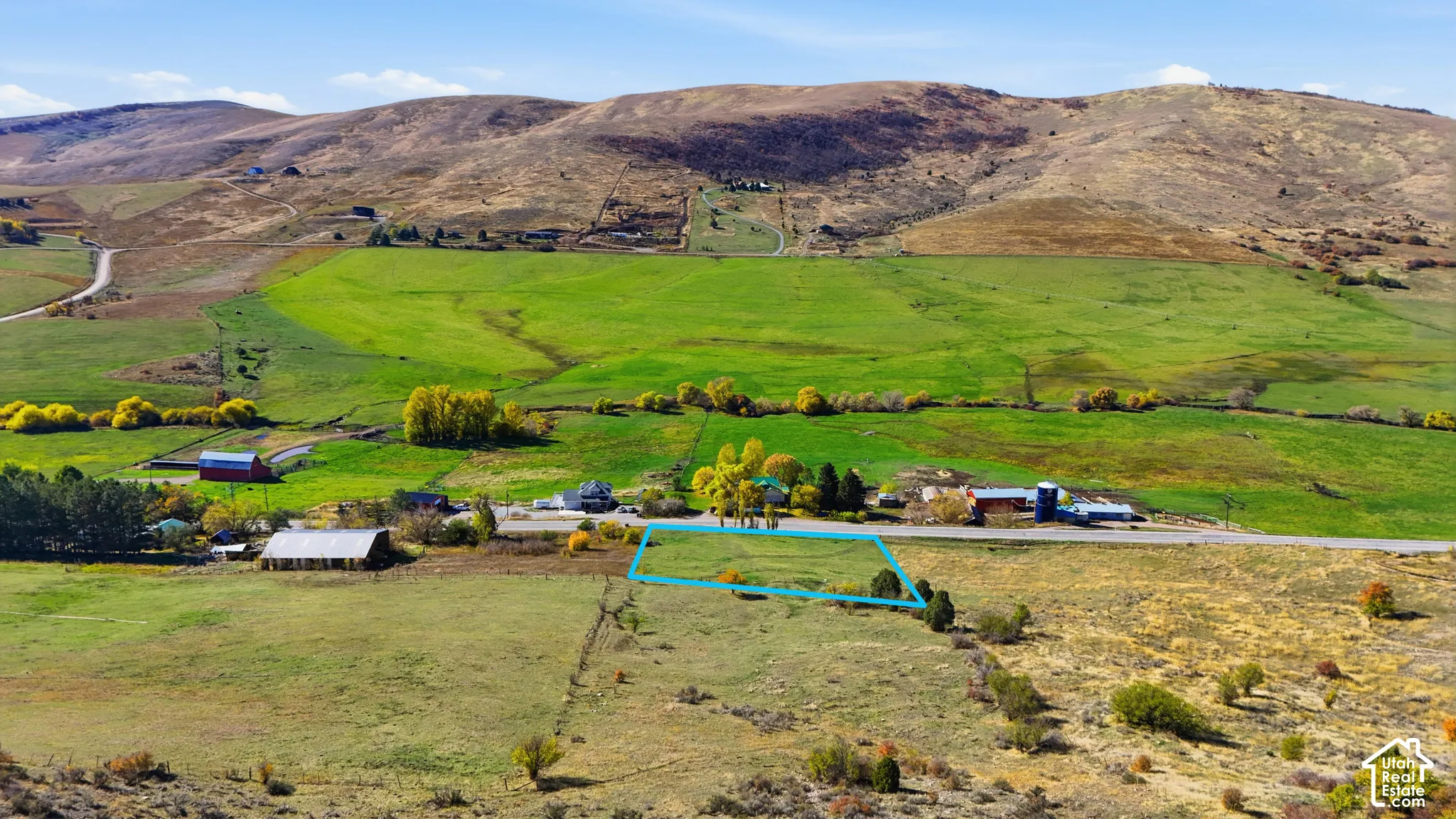 Aerial perspective of expansive open land parcel featuring mountain terrain, mature trees, and proximity to paved road access