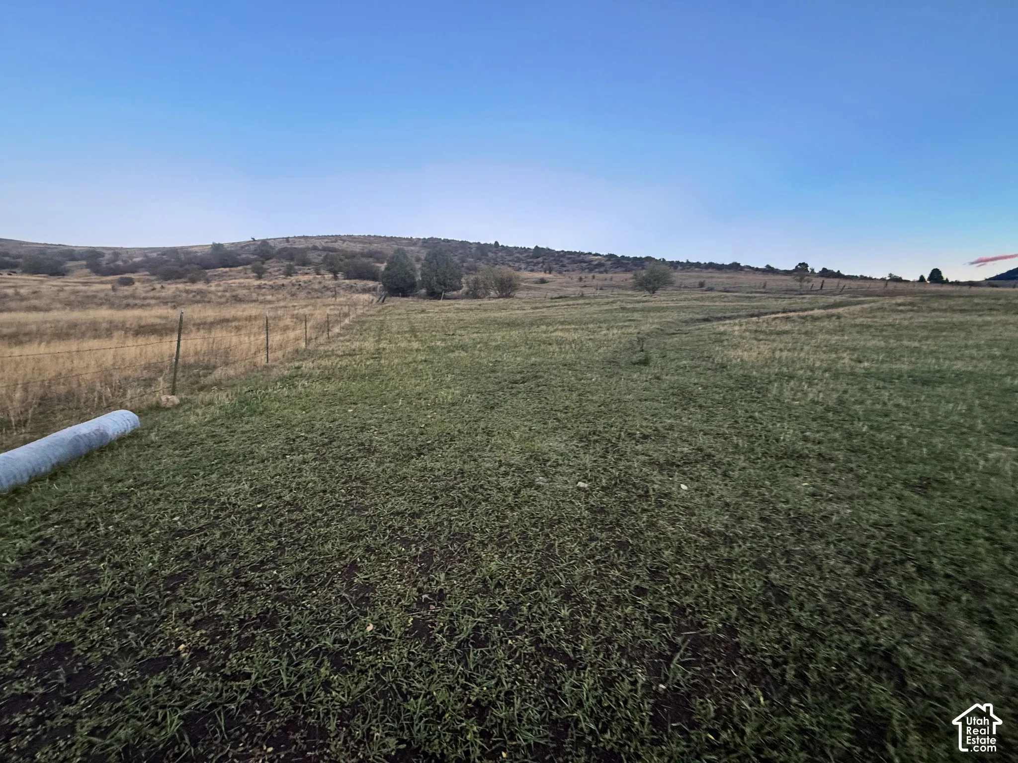 Expansive acreage featuring rolling terrain, native grasses, wire fencing, and mature trees against a mountain backdrop