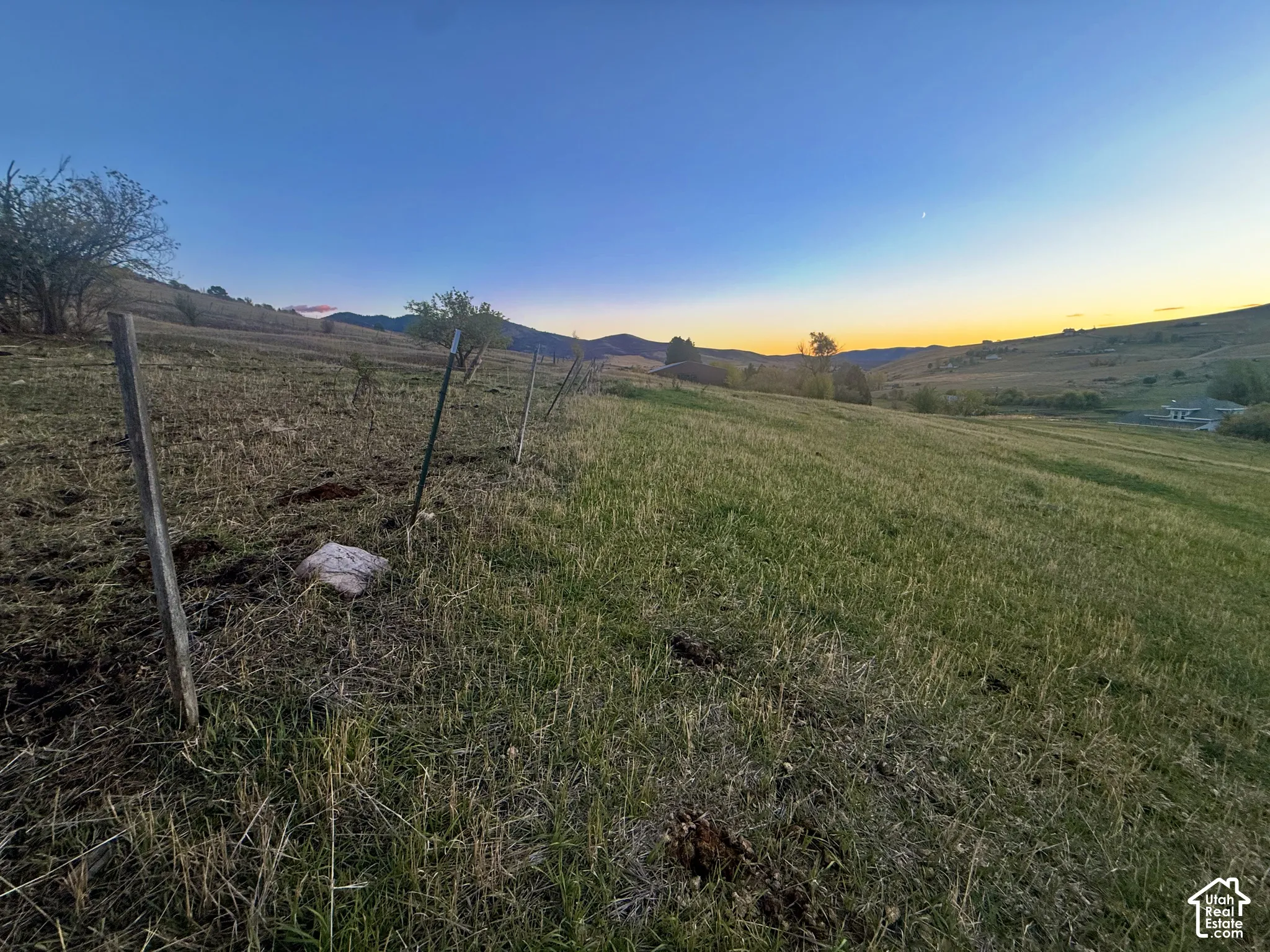 Expansive acreage featuring rolling grass terrain, mountain backdrop, and post-and-wire perimeter fencing