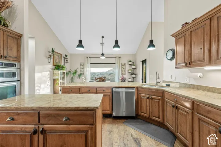 Kitchen featuring vaulted ceilings, wood-finish flooring, custom wood cabinetry, stone countertops, and stainless steel appliances