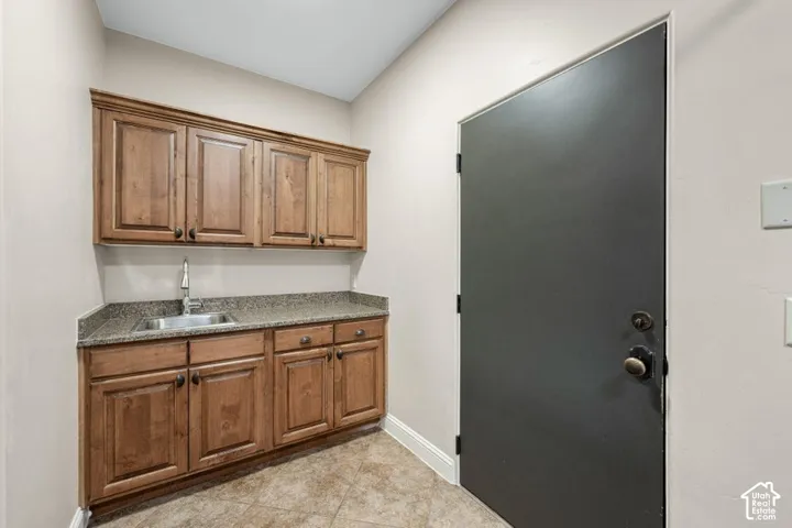 Integrated utility sink with a tall faucet, rich wood-finish cabinetry, speckled countertop, and tiled flooring