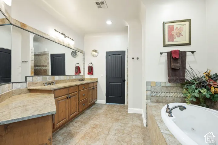 Dual wood-finish vanities with undermount sinks, a built-in soaking tub, a large framed mirror, and tile flooring