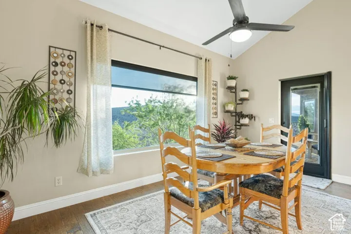Vaulted ceiling, ceiling fan with integrated lighting, wood-finish flooring, full-light exterior door, and an expansive window