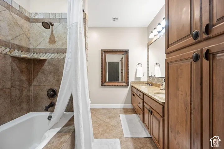 Bathtub with tile surround and bronze fixtures, dual vanity with stone countertop, wood-finish cabinetry, and built-in storage