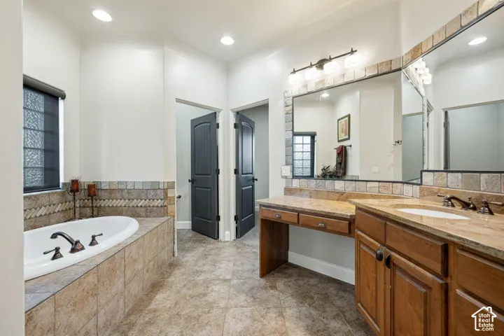 Expansive bathroom featuring a built-in soaking tub, dual vanity with integrated sink, wood cabinetry, and tiled flooring