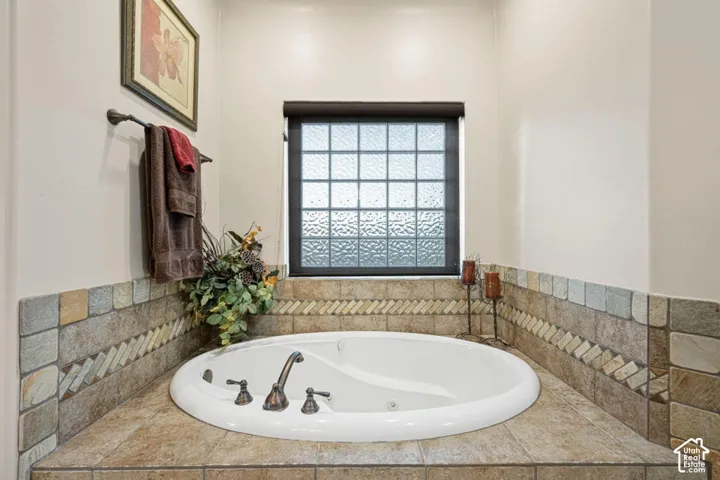 Built-in soaking tub with bronze-tone fixtures, surrounded by mixed-material tile and a privacy window
