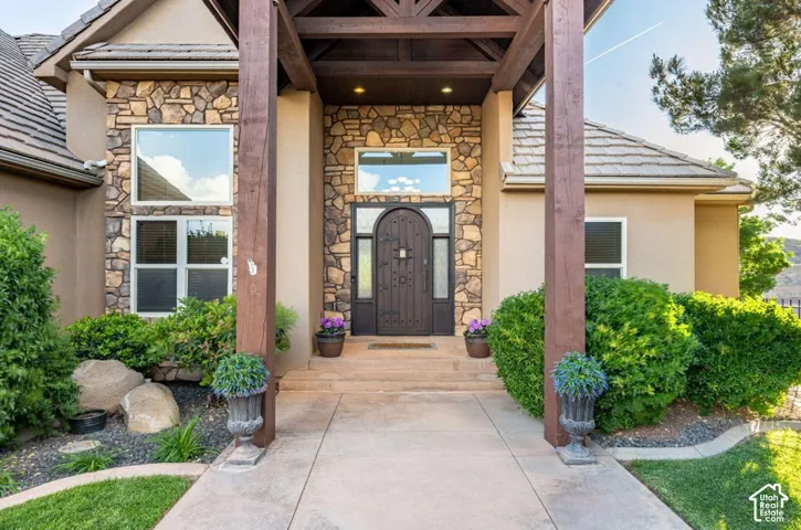 Stone and stucco exterior with an arched entry door, exposed beam portico, and mature landscaping