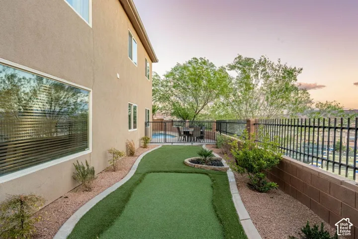 Exterior featuring a stucco finish, extensive artificial turf, a putting green, a black metal fence, and a block retaining wall