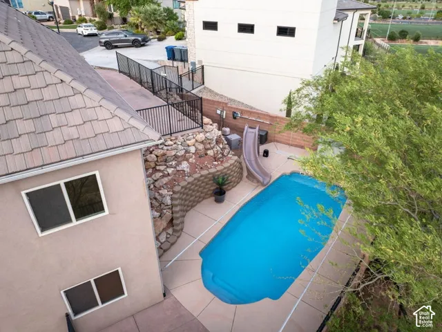 Rear exterior featuring a swimming pool, paved patio, retaining wall, and mature landscaping