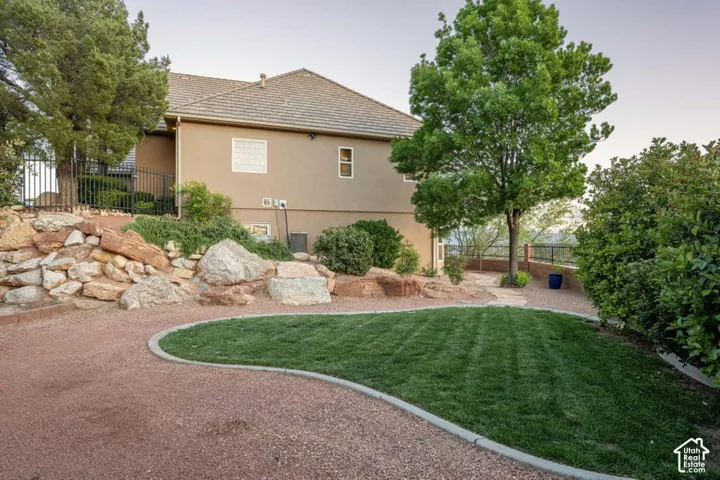 Expansive exterior featuring a stucco facade, a stone retaining wall, a gravel pathway, a manicured lawn, and mature trees