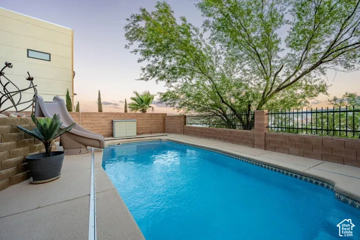 Concrete patio with a rectangular pool, block retaining wall, and wrought iron fencing