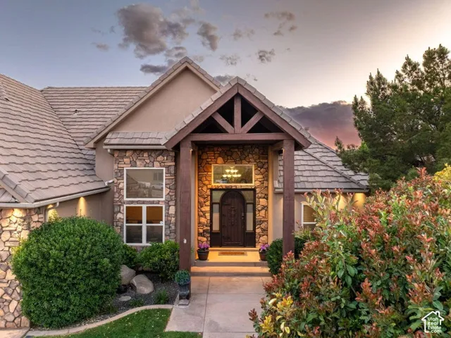 Stone veneer facade with stucco accents, gabled entryway with exposed timber, arched wood front door, and tiled roofing