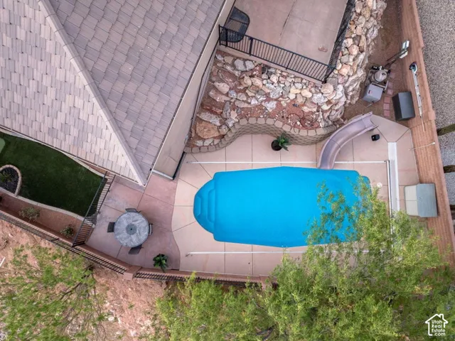 Backyard featuring a covered swimming pool with slide, a concrete patio, and a section of artificial turf