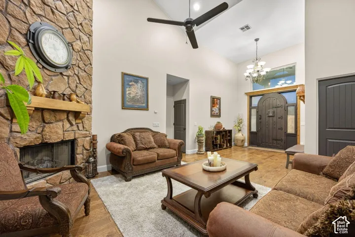 Vaulted ceilings with a ceiling fan, stone-clad fireplace with wood mantel, wood-finish flooring, and a decorative arched entry door with sidelights