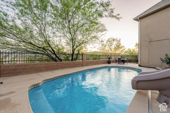 In-ground swimming pool with a concrete surround, block retaining wall, and black metal fencing