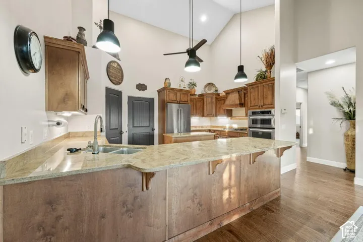 Vaulted ceilings with a ceiling fan, wood-finish flooring, undermount sink with a gooseneck faucet, light-toned countertops, and stainless steel double ovens