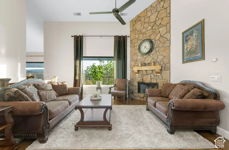 Vaulted ceilings, stone-faced fireplace with a wood mantel, wood-finish flooring, and a ceiling fan