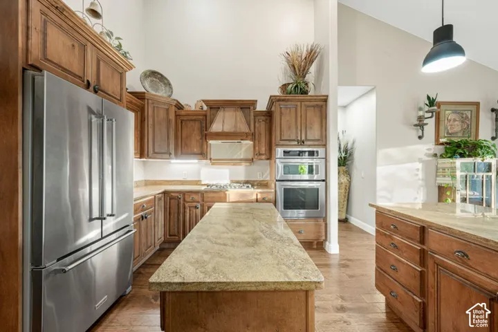 Kitchen featuring wood cabinetry, stainless steel appliances, a center island with a stone countertop, and wood-finish flooring