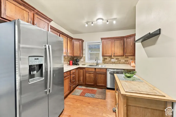 Kitchen featuring stained wood cabinetry, stainless steel appliances, neutral stone-finish countertops, tiled backsplash, and wood-finish flooring