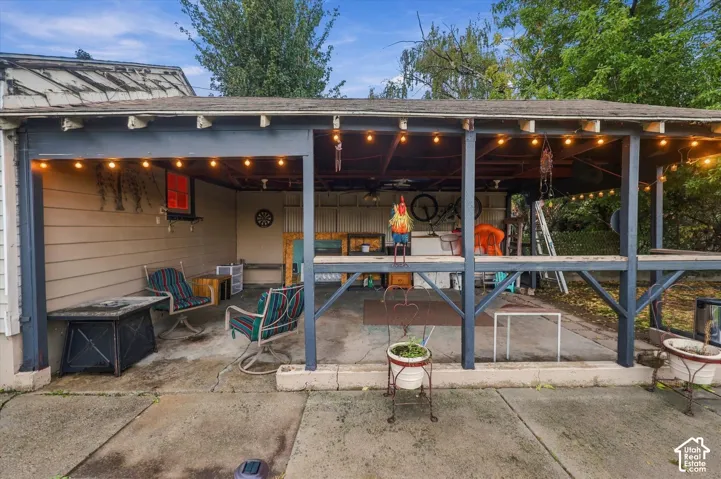 Covered concrete patio featuring horizontal wood siding, timber support beams, and built-in string lighting