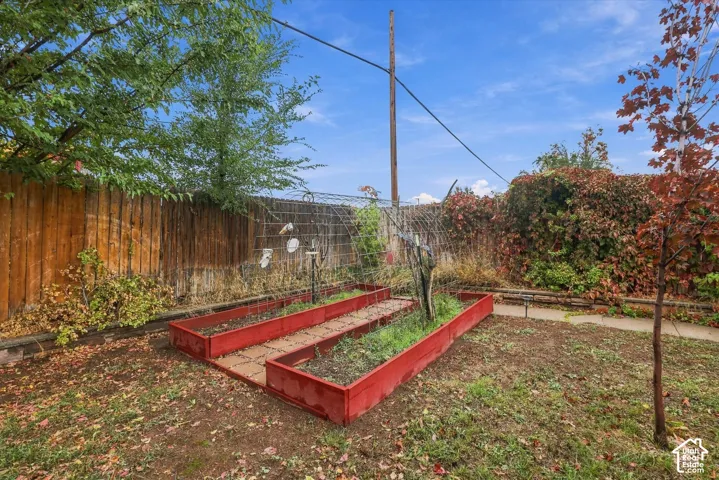 Outdoor area featuring raised garden beds, a metal trellis, wood-panel fencing, and mature trees