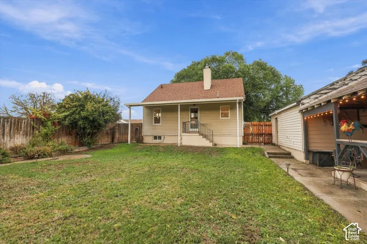 Rear exterior featuring a covered patio, chimney, metal staircase, lawn area, and perimeter wood fencing