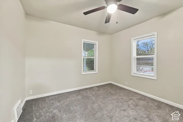 Neutral-toned interior space featuring wall-to-wall carpeting, two dual-pane windows with horizontal blinds, and a central ceiling fan with integrated light fixture