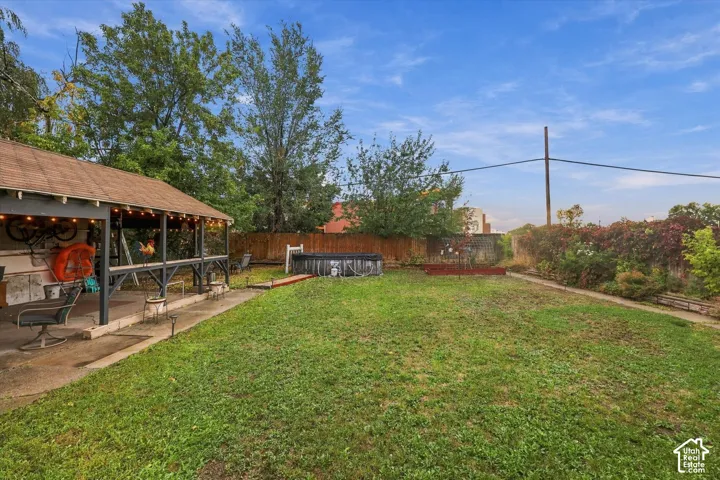 Backyard featuring a covered patio, grass lawn, wood fence perimeter, and mature trees