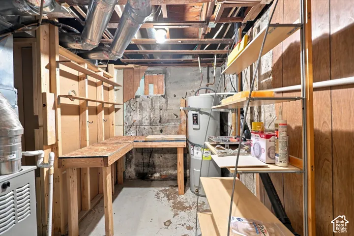 Utility space featuring exposed ceiling joists, concrete masonry walls, a built-in wood-frame workbench, and a water heater