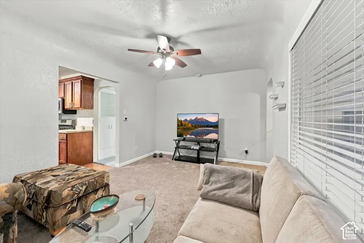 Living area featuring neutral wall tones, wall-to-wall carpeting, an arched doorway, and a ceiling fan with integrated lighting