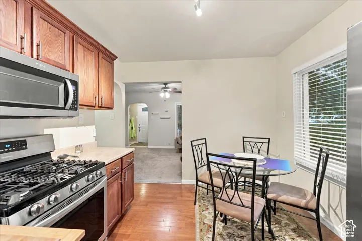 Kitchen featuring wood-finish cabinetry, stainless steel gas range, built-in microwave, wood-finish flooring, and horizontal window blinds