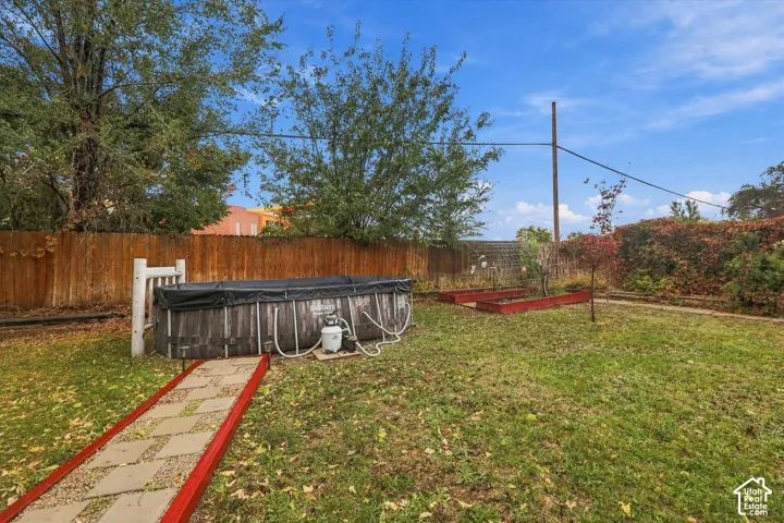 Backyard featuring a wood-fenced perimeter, elevated garden beds with red borders, and a stone-paver walkway