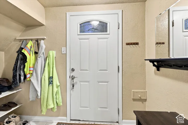 Entry area featuring a white four-panel door with an arched decorative glass insert, built-in shelving, wall-mounted wooden hooks, and a rectangular wall mirror with an integrated shelf