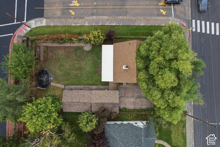 Corner lot property featuring an asphalt-shingled roof, an attached patio cover, mature trees, and an open grass area