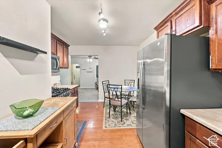 Kitchen featuring stained wood cabinetry, stainless steel side-by-side refrigerator, gas range, wood-finish flooring, and track lighting