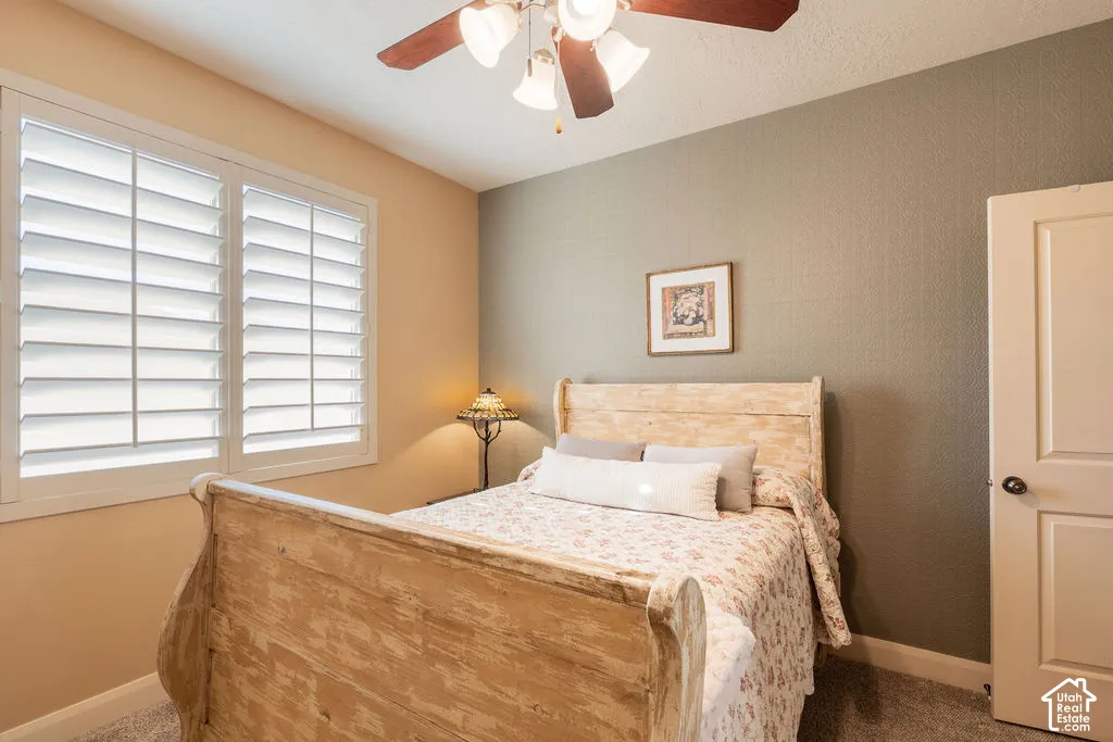 Window with plantation shutters, ceiling fan with integrated lighting, paneled door, and textured wall finish