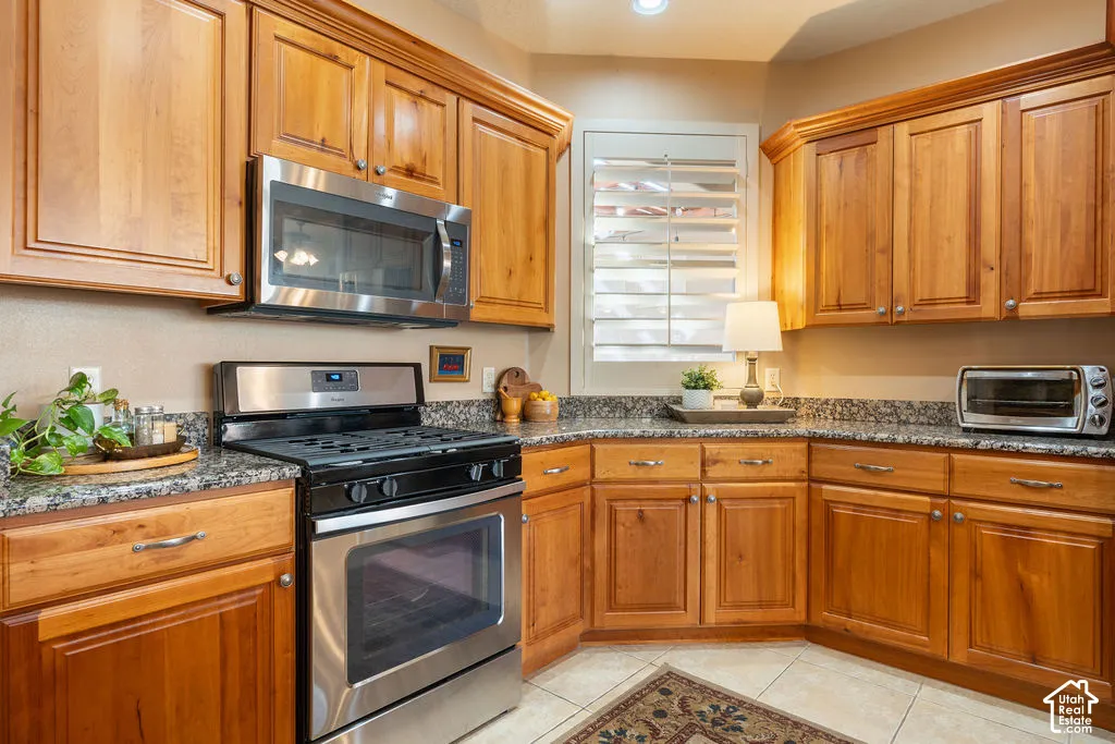 Wood cabinetry with crown molding, stainless steel appliances, granite countertops, tile flooring, and a window with plantation shutters