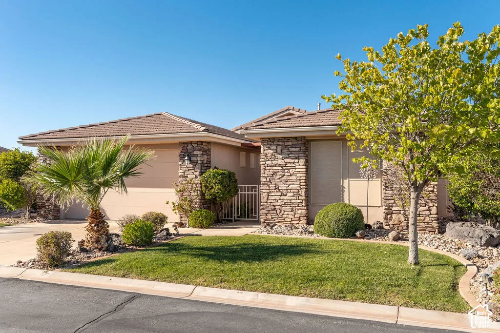 Stone facade accents, tile roofing, manicured lawn, established landscaping, and paved driveway