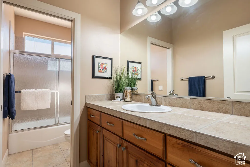 Warm wood-finish cabinetry with silver-tone hardware, a drop-in sink, and a tiled countertop with a matching backsplash
