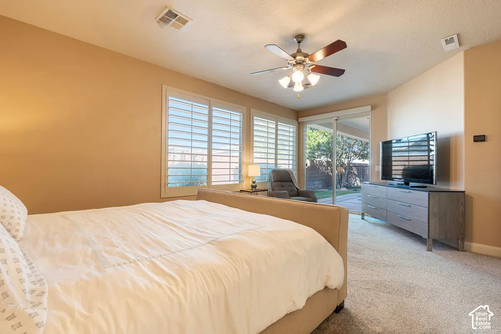 Neutral-toned carpeting, ceiling fan with integrated lighting, plantation shutters, and sliding glass door leading to outdoor space