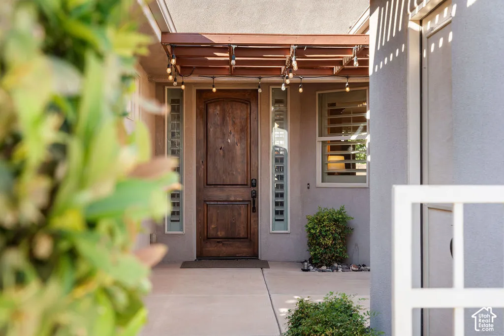 Wood-paneled front door, wood pergola entry, vertical window panels, window with horizontal blinds, stucco exterior