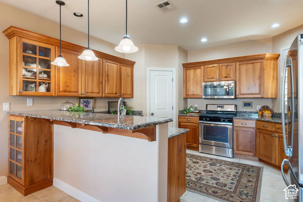 Kitchen featuring wood cabinetry, granite countertops, stainless steel appliances, and pendant lighting