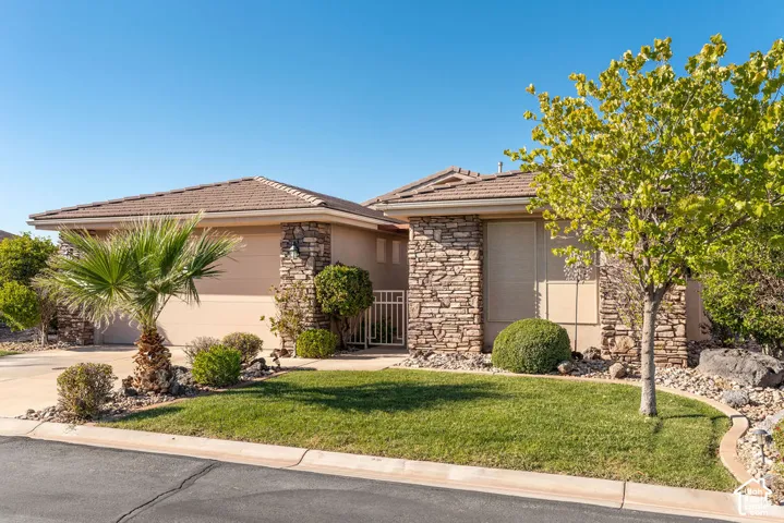 Stone facade accents, tile roofing, manicured lawn, established landscaping, and paved driveway