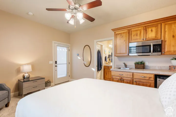 Wood-finish ceiling fan with integrated lighting, wood cabinetry with stainless steel microwave, built-in wet bar with sink, and carpeted flooring