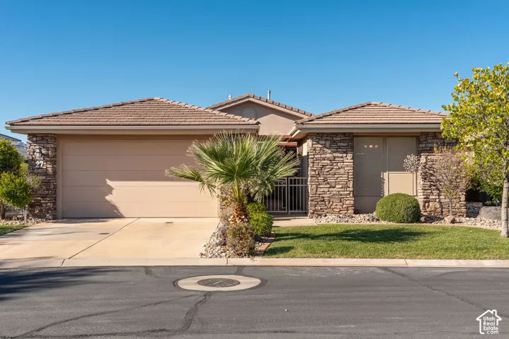 Exterior featuring a tiled roof, stacked stone facade, attached garage, concrete driveway, and front lawn