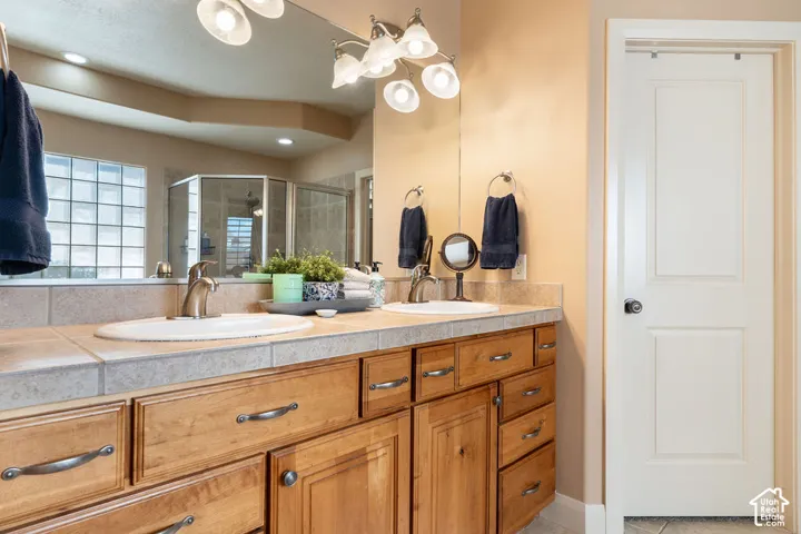 Dual vanity with natural wood-finish cabinetry, tile countertop, and brushed nickel fixtures