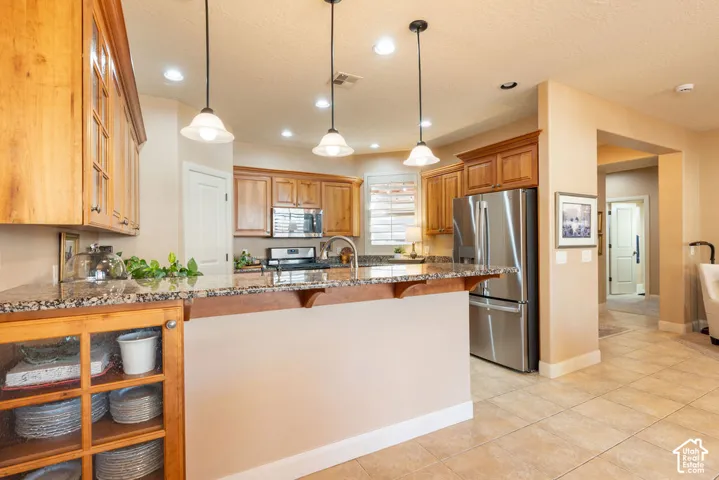 Kitchen featuring granite-style countertops, wood cabinetry, stainless steel appliances, and pendant lighting