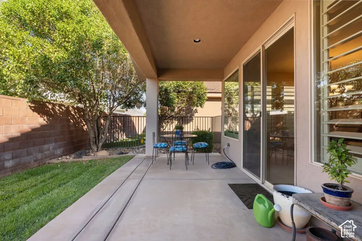 Covered patio with concrete flooring, mature trees, a brick wall, and sliding glass doors