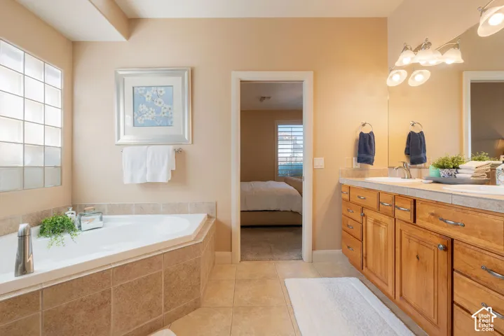 Corner soaking tub with tile surround, glass block window, double vanity with wood cabinetry, and dual undermount sinks