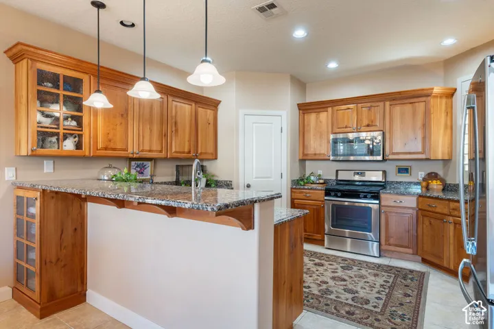 Kitchen featuring wood cabinetry, granite countertops, stainless steel appliances, and pendant lighting